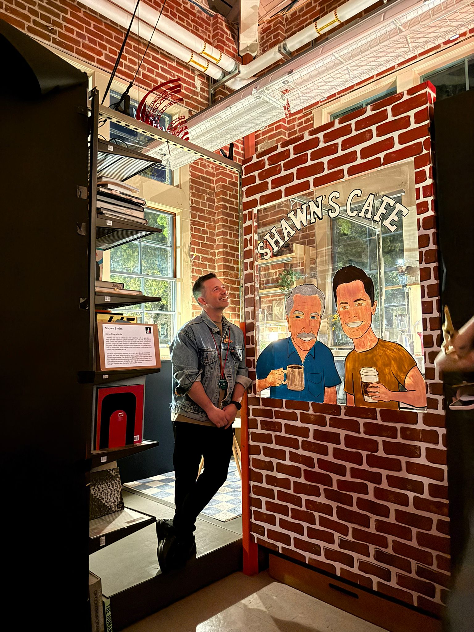 Shawn beside the hand-painted Shawn's Café brick-wall mural at the Stanford d.school